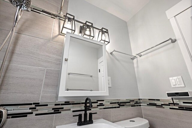 bathroom with a sink, a wainscoted wall, toilet, vaulted ceiling, and tile walls