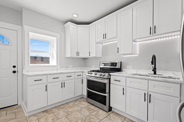 kitchen featuring light stone counters, white cabinets, a sink, range with two ovens, and recessed lighting