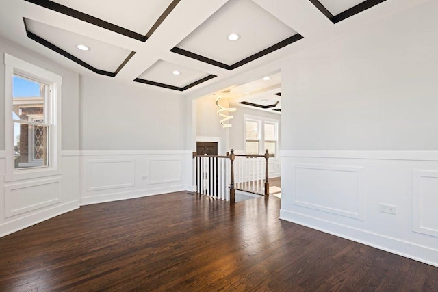 empty room featuring beamed ceiling, a decorative wall, coffered ceiling, wood finished floors, and wainscoting
