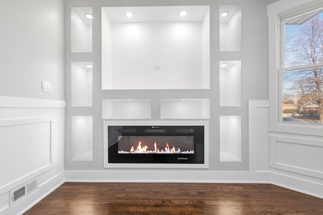 details featuring built in shelves, visible vents, wood finished floors, and a glass covered fireplace