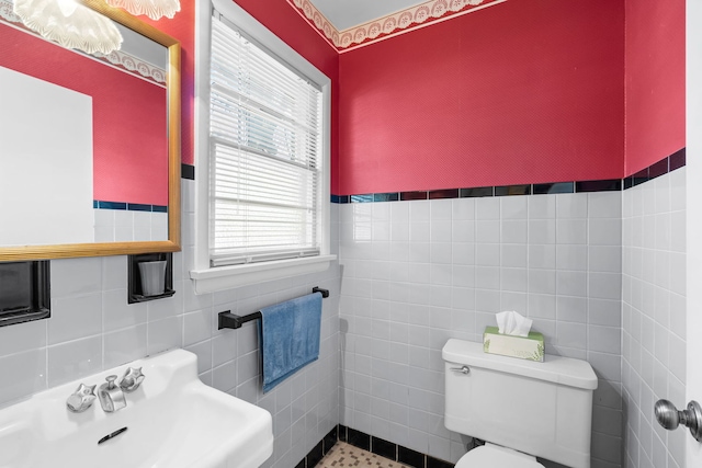 bathroom featuring toilet, tile walls, and a sink
