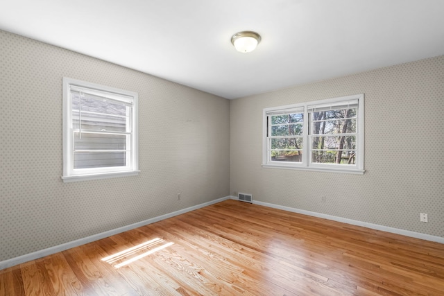 spare room with baseboards, visible vents, wood finished floors, and wallpapered walls