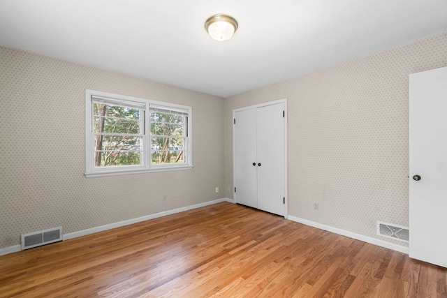unfurnished bedroom featuring visible vents, light wood finished floors, wallpapered walls, and baseboards