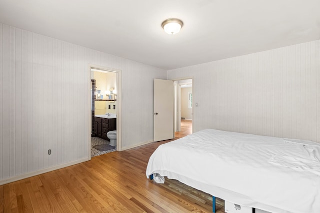 bedroom with ensuite bathroom, light wood-style flooring, and baseboards
