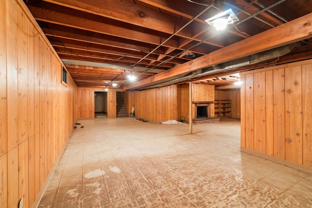finished below grade area featuring wood walls, tile patterned floors, a brick fireplace, and stairs