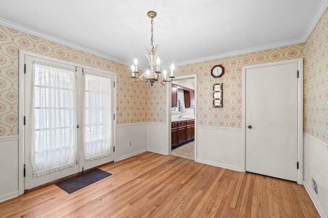 unfurnished dining area featuring ornamental molding, light wood finished floors, a wainscoted wall, and a notable chandelier