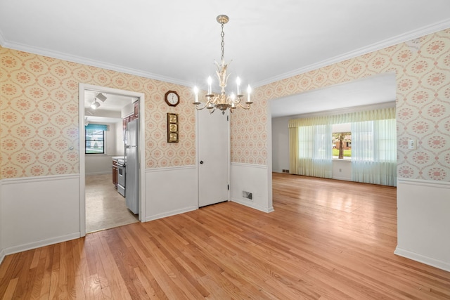 unfurnished dining area with wallpapered walls, a wainscoted wall, light wood-type flooring, a notable chandelier, and crown molding