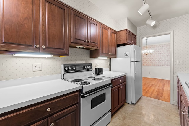 kitchen featuring light countertops, wallpapered walls, track lighting, white appliances, and a notable chandelier