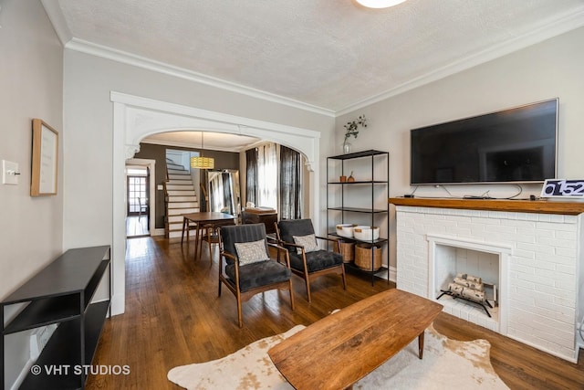 living room with a textured ceiling, arched walkways, a brick fireplace, wood finished floors, and stairs