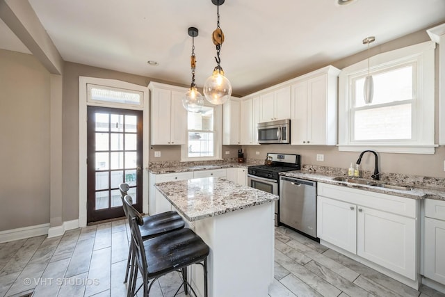 kitchen with a breakfast bar, a sink, stainless steel appliances, white cabinetry, and a kitchen island