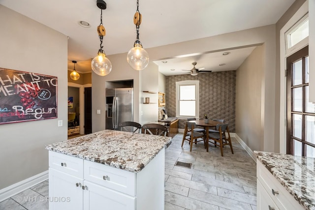 kitchen featuring a ceiling fan, baseboards, white cabinets, stainless steel fridge, and an accent wall