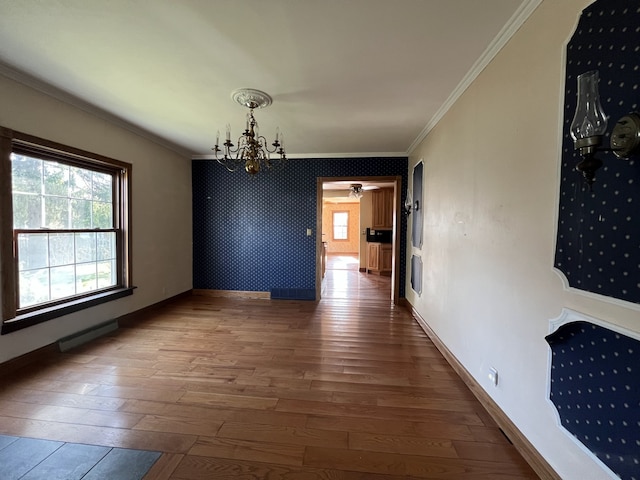unfurnished dining area featuring crown molding, a chandelier, hardwood / wood-style flooring, and baseboards