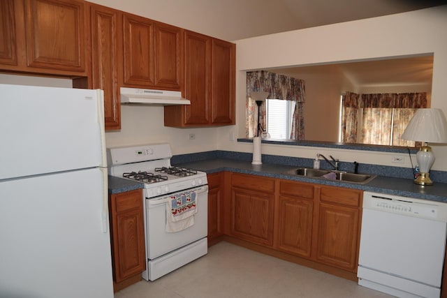 kitchen featuring white appliances, under cabinet range hood, brown cabinets, dark countertops, and a sink