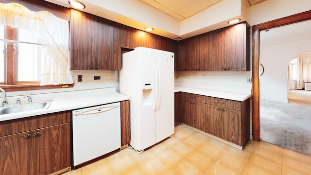 kitchen with white appliances, arched walkways, a sink, backsplash, and light countertops
