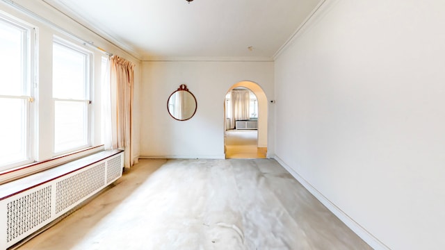 spare room with arched walkways, ornamental molding, radiator, light carpet, and baseboards