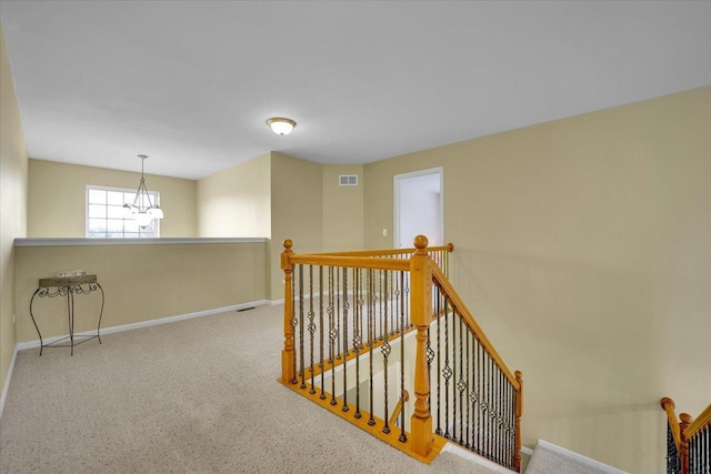 corridor featuring a chandelier, visible vents, carpet floors, baseboards, and an upstairs landing