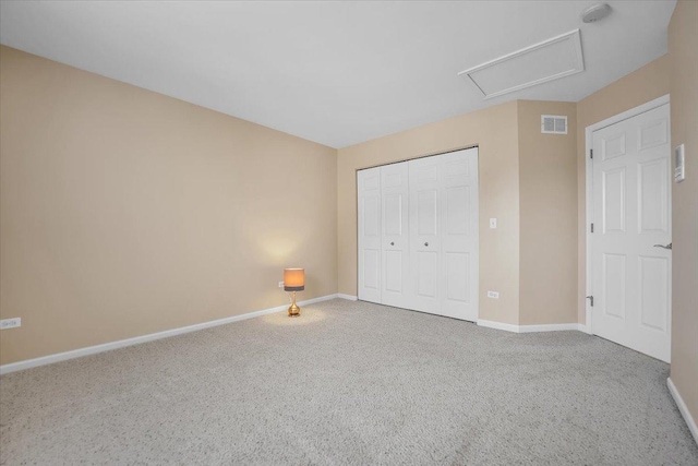 unfurnished bedroom with attic access, visible vents, carpet floors, baseboards, and a closet