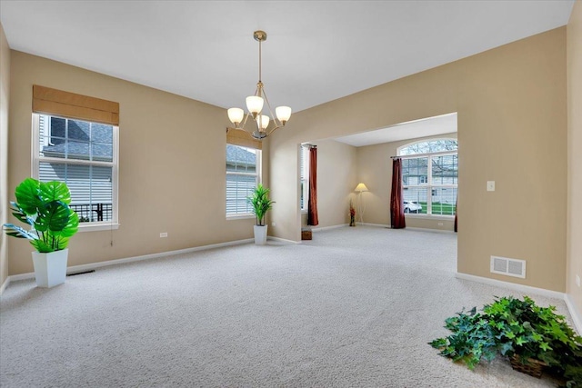 empty room with an inviting chandelier, plenty of natural light, carpet flooring, and visible vents