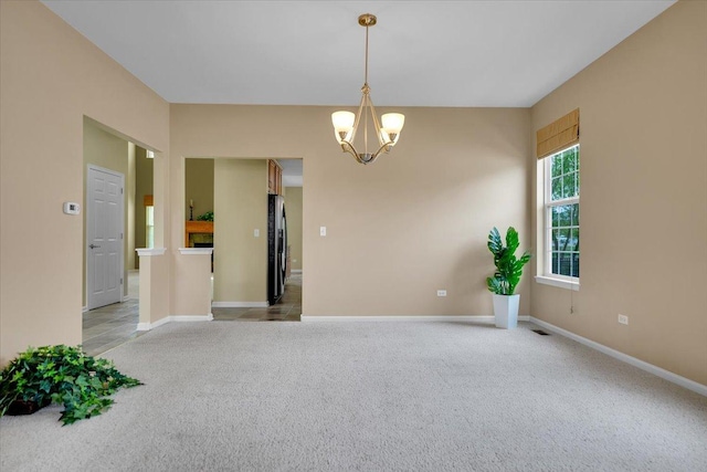 carpeted empty room featuring baseboards and a chandelier