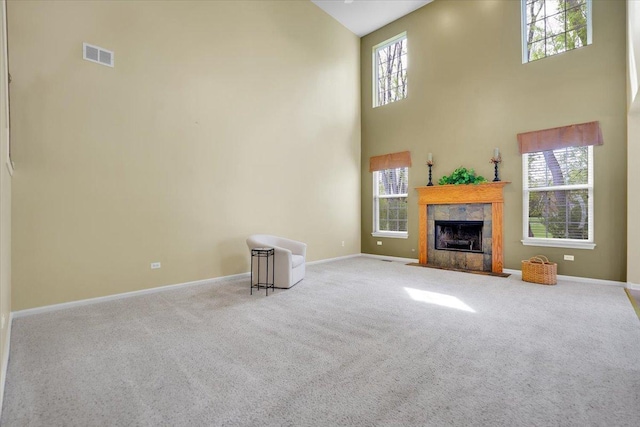 unfurnished living room with visible vents, a towering ceiling, a fireplace, baseboards, and carpet