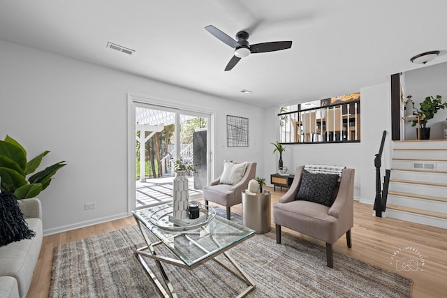 living room with stairway, a ceiling fan, visible vents, baseboards, and wood finished floors
