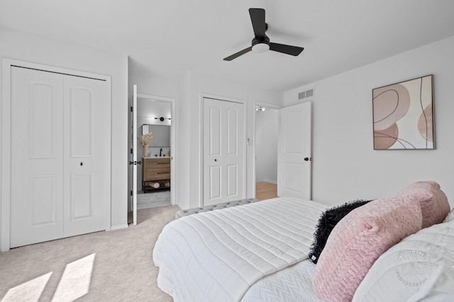 bedroom featuring connected bathroom, carpet, multiple closets, visible vents, and a ceiling fan