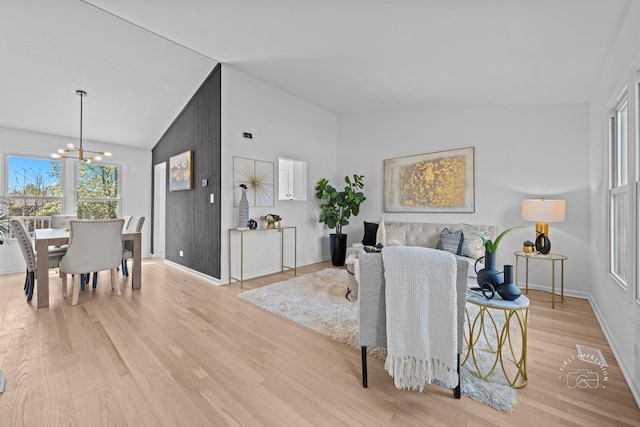 living area with light wood finished floors, a notable chandelier, high vaulted ceiling, and baseboards