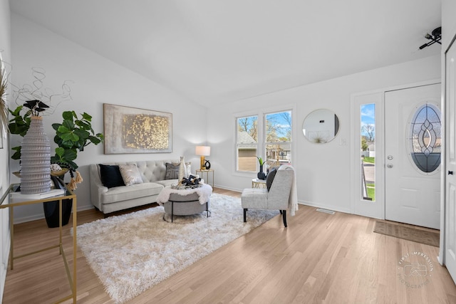 living area with visible vents, light wood-type flooring, vaulted ceiling, and baseboards