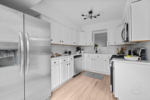 kitchen with decorative backsplash, light wood-style floors, appliances with stainless steel finishes, light countertops, and white cabinetry