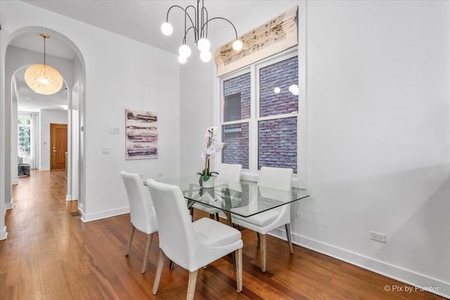 dining space with arched walkways, baseboards, and wood finished floors