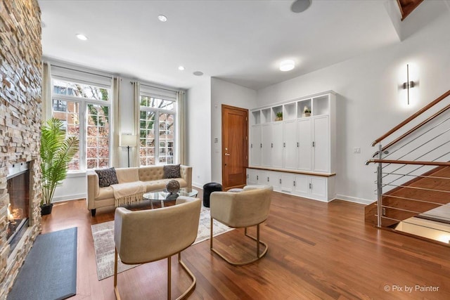 living area featuring a stone fireplace, baseboards, stairs, and wood finished floors