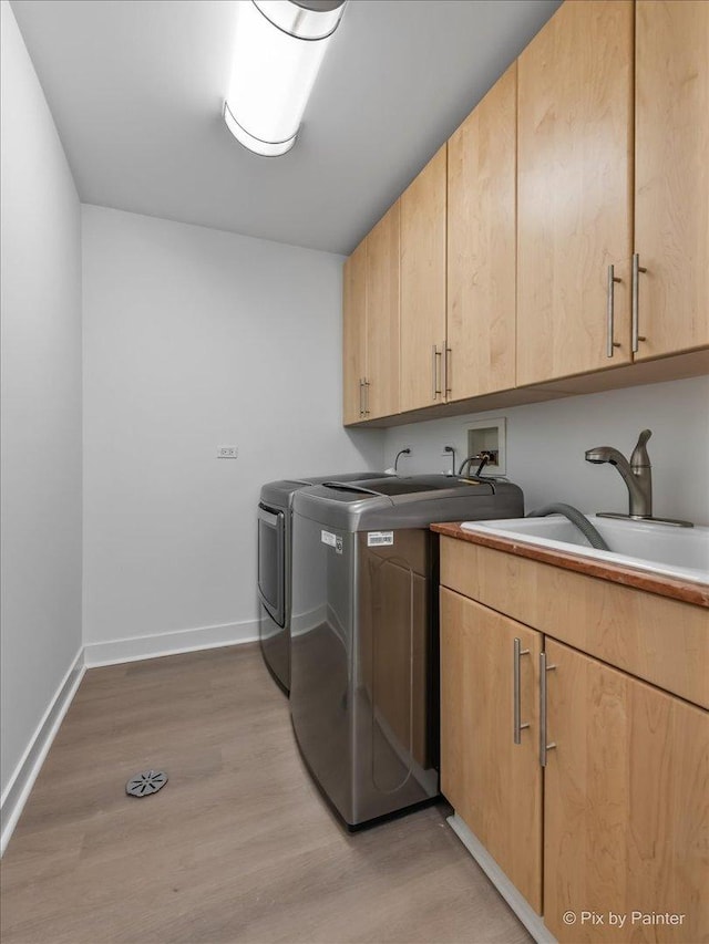 clothes washing area featuring cabinet space, a sink, baseboards, light wood-style flooring, and washer and dryer