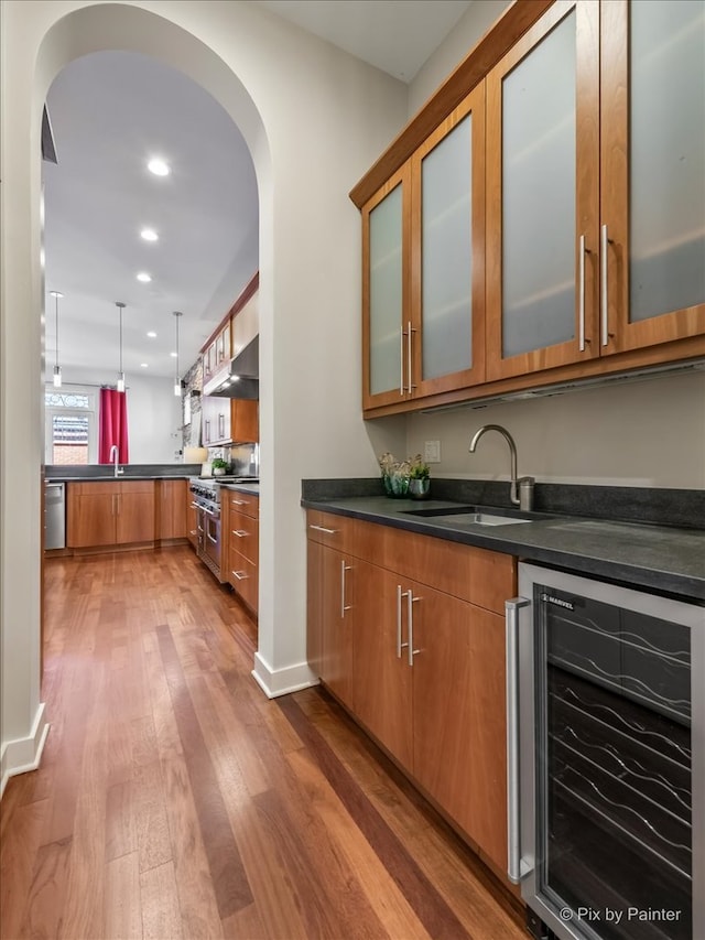 bar featuring beverage cooler, arched walkways, under cabinet range hood, a sink, and appliances with stainless steel finishes