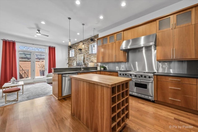 kitchen with wall chimney range hood, appliances with stainless steel finishes, a sink, wooden counters, and a peninsula