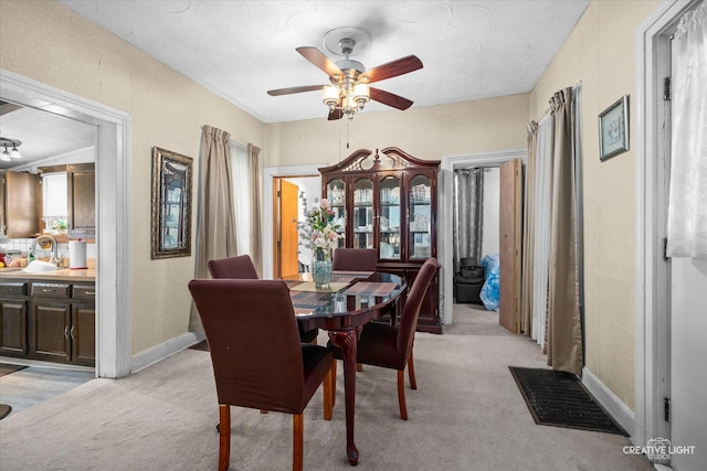dining space featuring a ceiling fan, light carpet, and baseboards