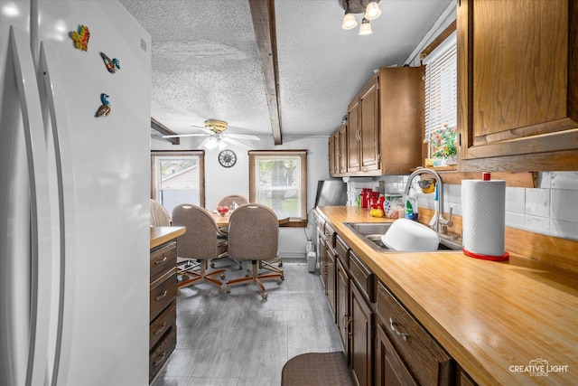 kitchen featuring freestanding refrigerator, a sink, butcher block countertops, a textured ceiling, and ceiling fan