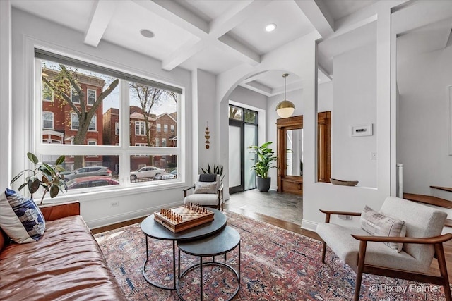living room with arched walkways, baseboards, wood finished floors, beamed ceiling, and coffered ceiling