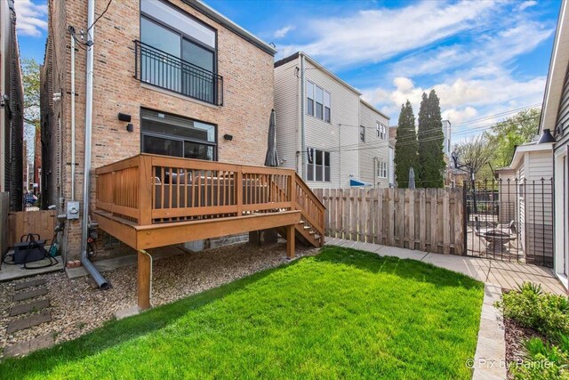 rear view of property with a wooden deck, fence, brick siding, a yard, and stairway