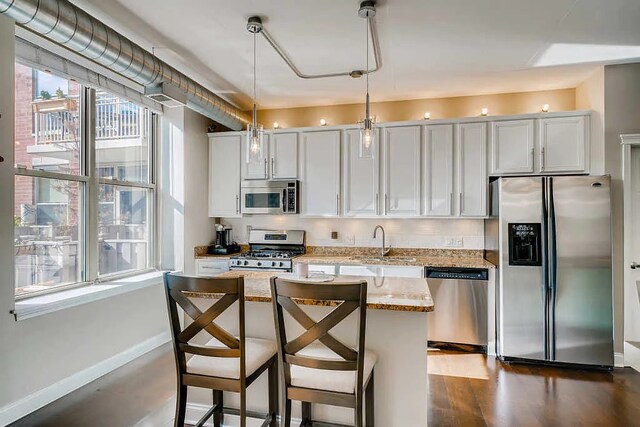 kitchen with a kitchen island, hanging light fixtures, a sink, baseboards, and stainless steel appliances