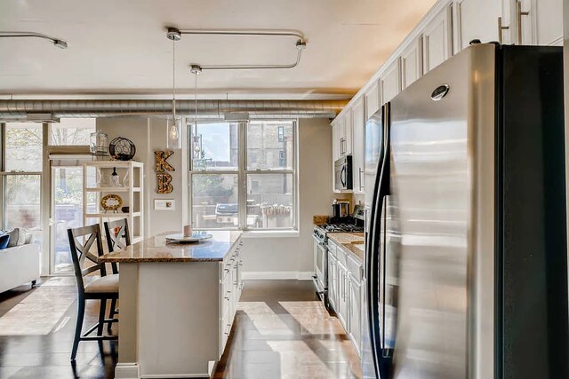 kitchen featuring stone countertops, appliances with stainless steel finishes, white cabinets, and a breakfast bar