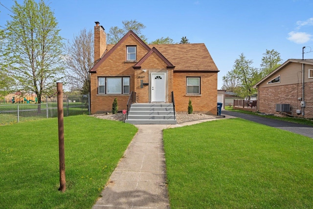 bungalow-style home featuring fence, central AC, a front lawn, brick siding, and a chimney