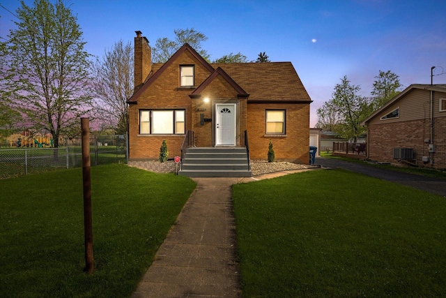 view of front of home with a chimney, a front yard, brick siding, fence, and cooling unit