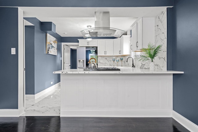 kitchen featuring a peninsula, baseboards, white cabinets, island exhaust hood, and appliances with stainless steel finishes
