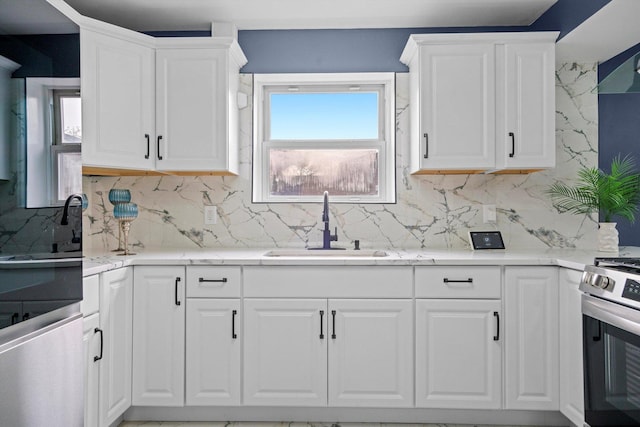 kitchen featuring a sink, backsplash, white cabinets, and gas range