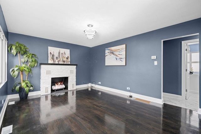 unfurnished living room featuring baseboards, visible vents, a stone fireplace, and wood finished floors