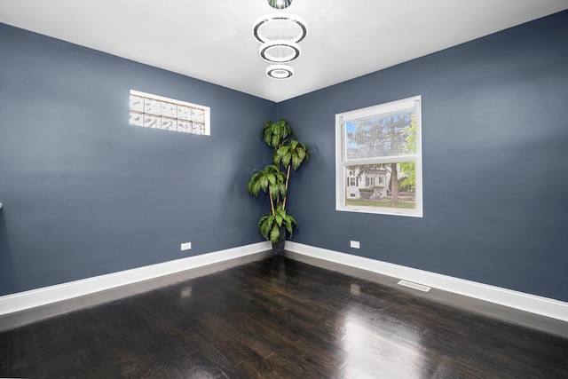 empty room featuring baseboards, visible vents, a healthy amount of sunlight, and wood finished floors