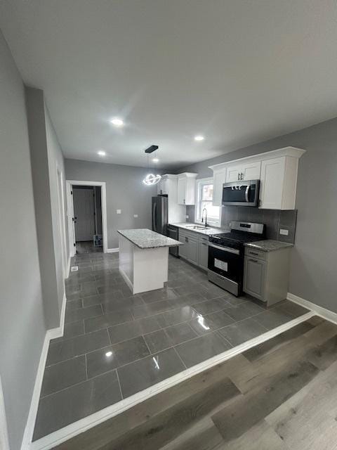kitchen featuring a sink, stainless steel appliances, white cabinetry, a kitchen island, and baseboards