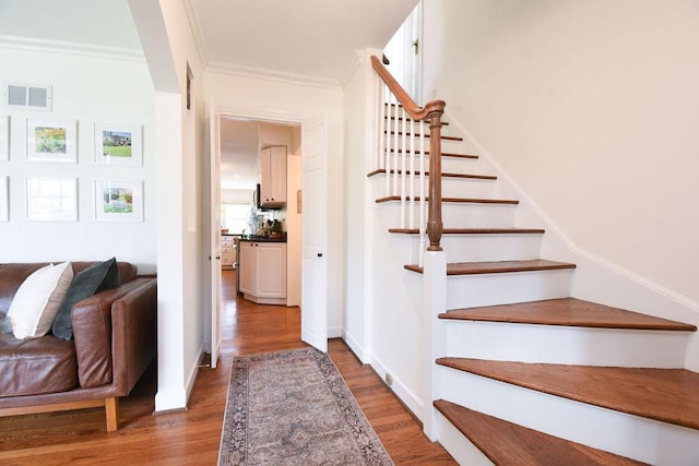 stairs with crown molding, baseboards, visible vents, and wood finished floors