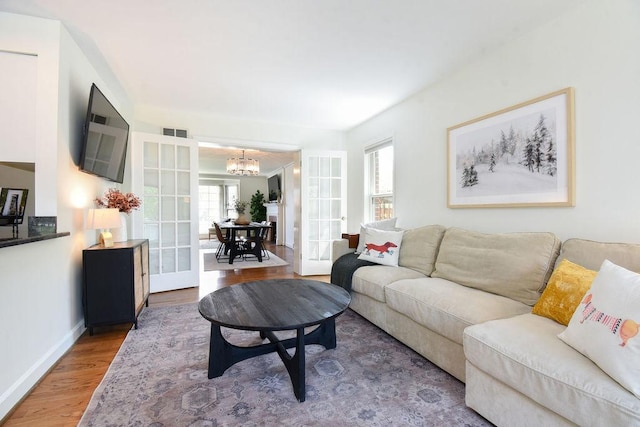 living room featuring a chandelier, french doors, baseboards, wood finished floors, and visible vents