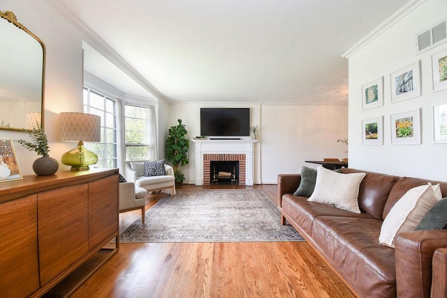 living area with visible vents, light wood-style floors, crown molding, and a fireplace
